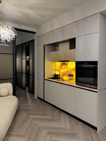 A stylish kitchen features minimalist cabinetry and a bright yellow backsplash, creating a vibrant focal point in a modern apartment. The open layout enhances the space's functionality and appeal.の写真素材
