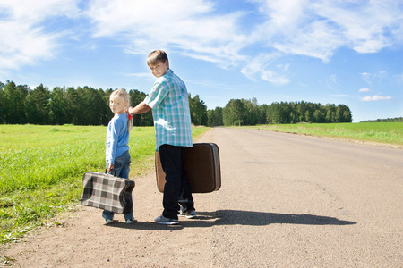  cute girl and boy with suitcase on roadの写真素材