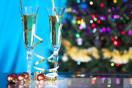 Two glass with champagne in blue style on table.  Christmas tree on  background.の写真素材