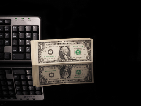 Dollar bills and keyboard on a black background with reflection.の写真素材