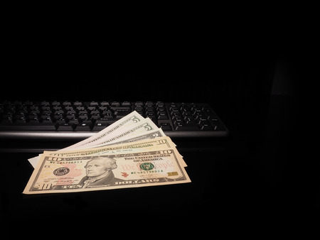 Dollar bills and keyboard on a black background with reflection.