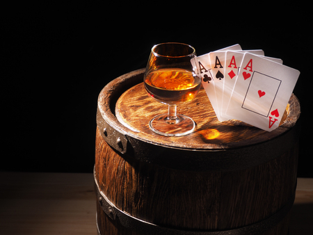 Playing cards and wine glass of cognac on barrel.の写真素材