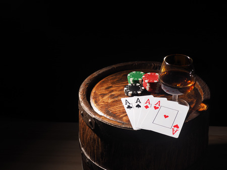Playing cards and wine glass of cognac on barrel.
