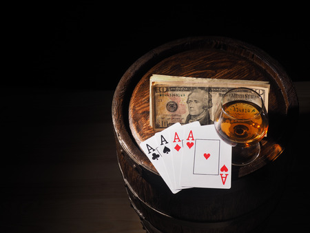 Playing cards and wine glass of cognac on barrel.