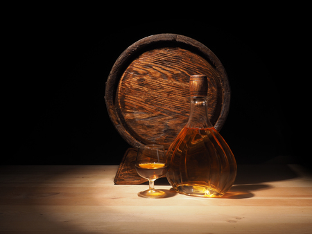 Glass of cognac with barrel on wooden backgroun.