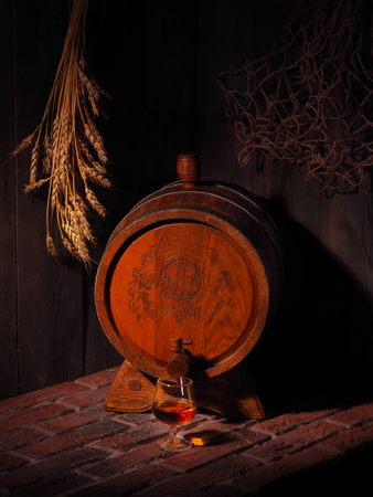 Glass of cognac with barrel in cozy cellar.の写真素材