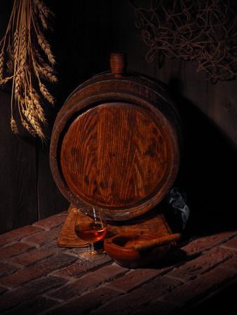 Glass of cognac with barrel in cozy cellar.の写真素材