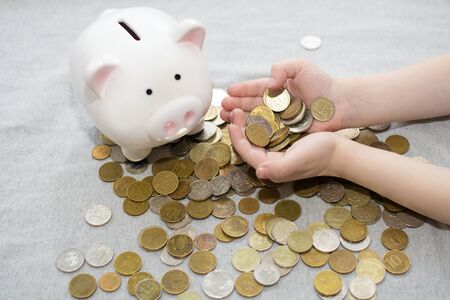 A lot of coins in childrens hands. Nearby is a piggy bank in the shape of a prosenka. Photo cropped, close upの写真素材