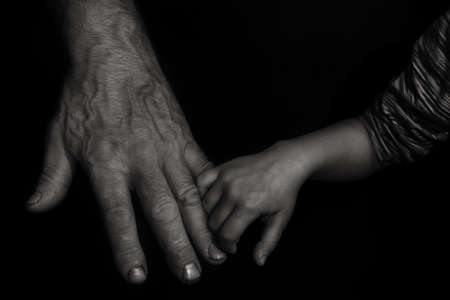 A small child's pen is holding a finger of a man's hand. The concept of grandfather and grandson, the connection of generations, support and transfer of experience. Photo black and white, processed. Close-upの写真素材