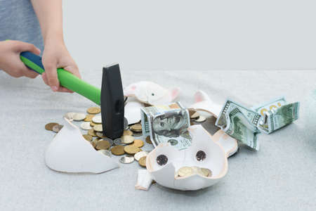 close-up of childrens hands holding a hammer smash a piggy bank. Coins and hundred dollar bills...
