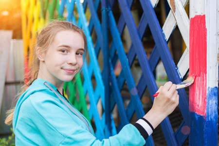 cute girl draws a fence on the street in the colors of the rainbow. Decorates the yard with a rosy...
