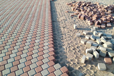 red and white paving stones and paving slabs are laid in even rows. There is a scattered pile of...