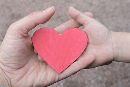 small wooden heart in the hand of a woman and a child. The concept is a mothers boundless love for a child, healing children, helping children. Horizontal photo, close-up.の写真素材