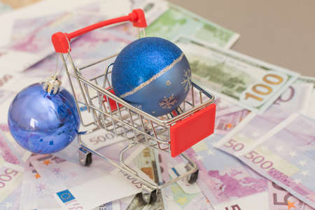 there is a blue christmas ball in the supermarket trolley. The cart is on euro and dollar bills. Concept - buying in an online store, delivering any product home, expenses, spending.の写真素材