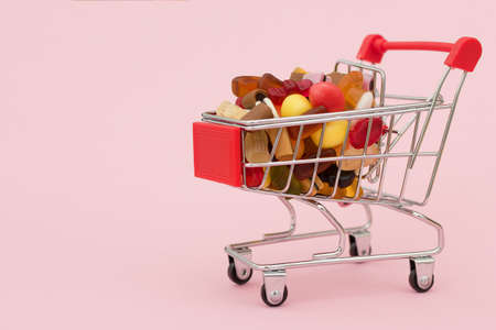 close-up of a small cart from on a pink background, filled with multicolored sweets and marmalade....