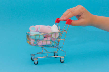 A toy grocery cart full of delicious little marshmallows is pushed by a child's hand. Photo in pastel colors, on a blue background, horizontal. Idea - purchase, delivery, selection, sweets and Goodies.の写真素材
