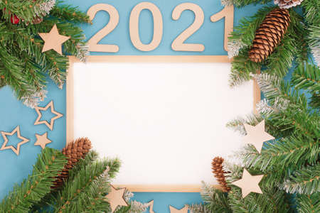 wooden photo frame on a blue background. It is surrounded by fir branches with wooden toys and the number 2021. The idea is a New Year's photo frame, a place for text, a template for advertisingの写真素材