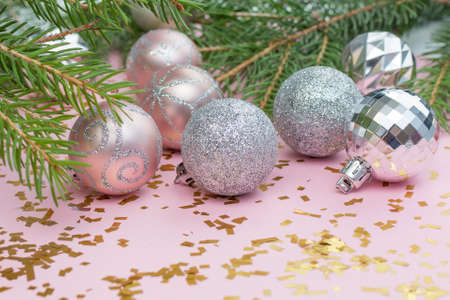 Silver and pink Christmas balls lie on a pastel pink background strewn with golden confetti and fir...