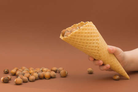 a waffle cone with a hazelnut in the childs hand, the cone is tilted and several nuts are poured out...