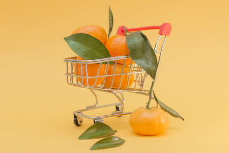 resh tangerines with leaves, in a cart from a supermarket, close-up, horizontal photo, yellow background. The idea is that you can buy fresh fruit from an online store, deliver goods to your homeの写真素材