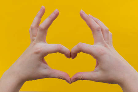 Close-up women's hands make the shape of the heart, on a yellow background. Horizontal photoの写真素材
