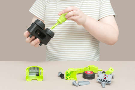 close-up of hands of a child using a screwdriver to assemble a toy car. The idea is that the child...
