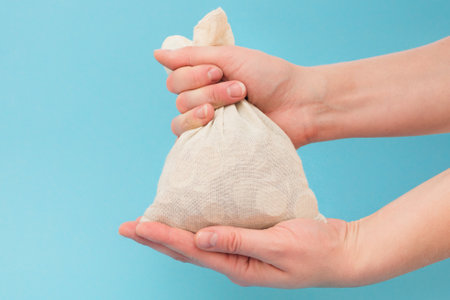 female hands hold a bag of coins on a blue background. Horizontal photo, close-upの写真素材