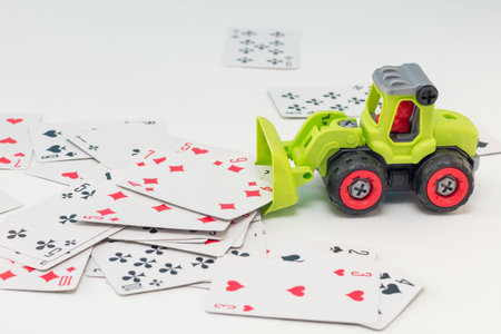 The toy tractor clears the white table from the playing cards. gorzontal photo, soft focus., white backgroundの写真素材