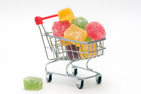 shopping cart filled with colored marmalade, on a white background. Horizontal photo, close-up. The idea is buying and selling sweets. Natural marmalade. Home delivery.の写真素材