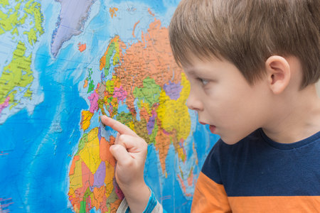 The child looks at the map of the world with concentration, enthusiasm. Close-up, horizontal photo. Idea - preschool education, study of geography, countries and continents.の写真素材