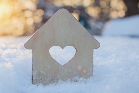 a small wooden house with a heart-shaped window stands on the snow. Concept - winter sales, buying or selling real estate, mortgages, affordable housing. Close-up, horizontal photoの写真素材
