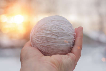 in a woman's hand a ball of white knitting threads, against the backdrop of a winter landscape and the sun. Horizontal photo. Idea - with creativity in life, creative people are everywhere.の写真素材