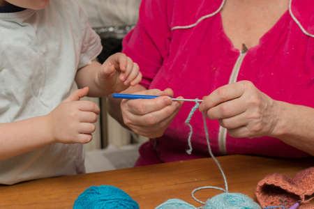 Grandmother teaches her grandson to crochet. Close-up of hands of grandmother and child. Horizontal photo. Concept - training, transfer of experience from the older generationの写真素材