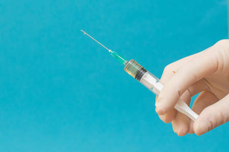 In a human hand a syringe with a medicine on a blue background. hands in medical sterile gloves....