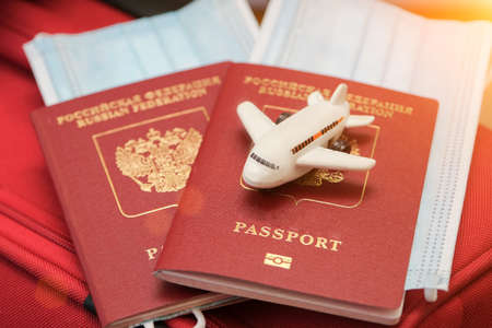 there are two passports on the red suitcase. The passports contain a medical mask and a small white toy plane. Concept - traveling, waiting for the opening of borders. Close-up, horizontal photo.の写真素材
