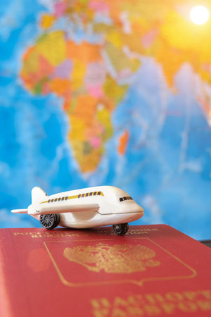 A toy little white airplane stands on a red passport on the background of the world map. Concept - travel. Vertical photo.の写真素材
