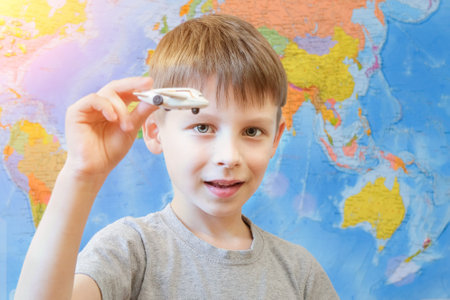 preschool boy with a toy airplane in his hands, on the background of the world map. The child looks into the camera. Concept - dreams of travel, summer vacation, the child is playing. Horizontal photoの写真素材