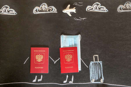 on the blackboard are two red Russian passports and a medical mask. Clouds, arms, legs and a suitcase are drawn in chalk. Concept - travel, tourism, vacation for two, vacation.の写真素材