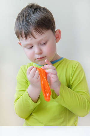 a boy of European appearance plays with orange slime. The child does not smile, he is looking at something. The concept is tactile sensations, the development of motor skills in children.の写真素材