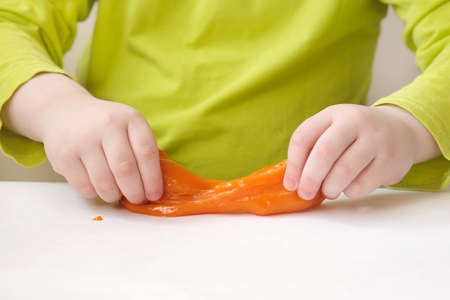 close-up of childrens hands stretching orange slime on a white table. The concept is the development of fine motor skills and tactile sensations in children. Horizontal photo.の写真素材