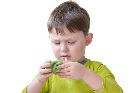 boy in green clothes plays with green soft plasticine. The child does not smile, is focused. Concept - educational games for children, development of creative thinking, fine motor skills.の写真素材