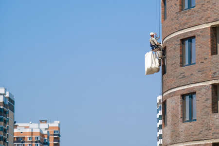 Industrial alpinism. A worker in a white helmet hangs on special equipment on the facade of a house...