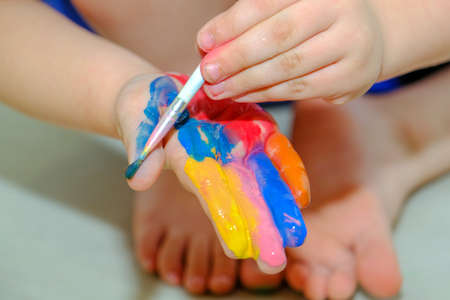 the child draws with paint on his hand with a brush. close-up. The idea is childrens creativity, self-expression, childrens development through drawing, classes with children. Foreground.の写真素材