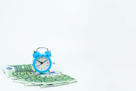 small blue clock on euro banknotes stands on a white background. The concept is time to make money,...
