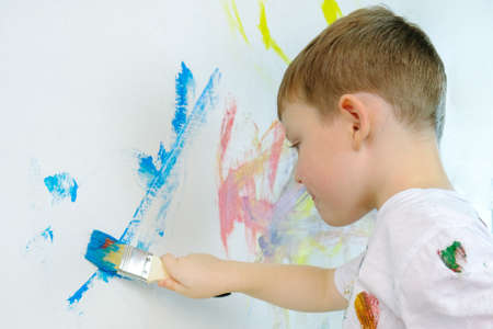 boy draws with a brush and blue paint on the wall. The child is engaged in childrens creativity with pleasure. horizontal photo, rear view.の写真素材