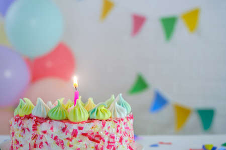cake with one lit candle, on the background of balloons and flags. Cake with red sprinkles and...