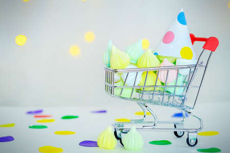 a minimalist supermarket trolley filled with sweets and decorated with a party hat. Buying sweets for a birthday, holiday, celebration. Home delivery of sweets.の写真素材
