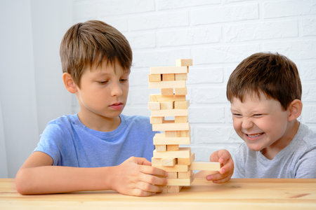 children play the board game , boys build a tower of wooden cubes, the concept of fine motor skills development, home joint games. Leisure for children at homeの写真素材