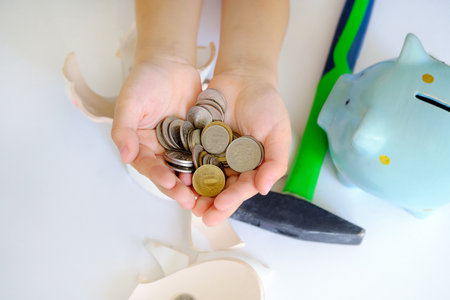 childrens palms hold coins, top view, close-up. broken piggy bank, hammer and piggy bank on the table. Idea - the child broke the piggy bank and took out his savings.の写真素材