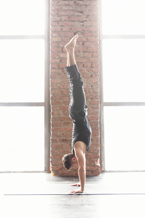Sport and yoga. Strong young athletic man doing exercise -Handstand against an urban background with...